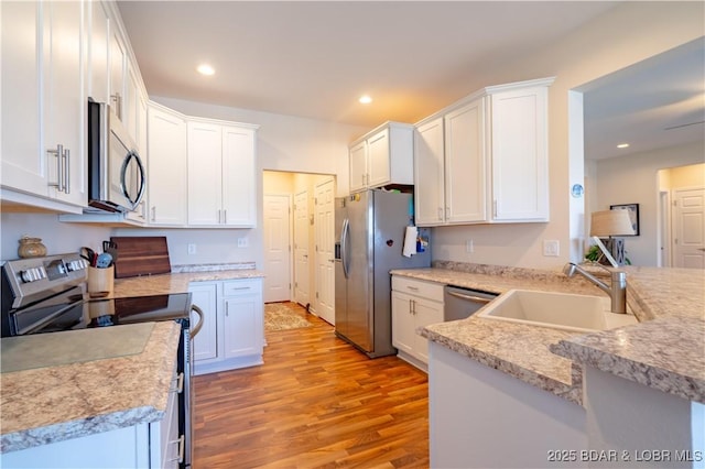 kitchen featuring appliances with stainless steel finishes, a sink, light wood-type flooring, white cabinets, and recessed lighting