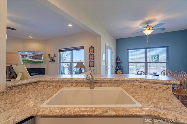 kitchen featuring a sink, a ceiling fan, recessed lighting, and a glass covered fireplace