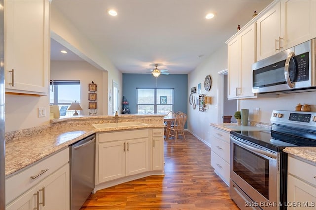 kitchen with appliances with stainless steel finishes, a sink, a peninsula, light wood-type flooring, and a ceiling fan