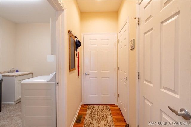 corridor with washer / clothes dryer, a sink, light wood-type flooring, and baseboards