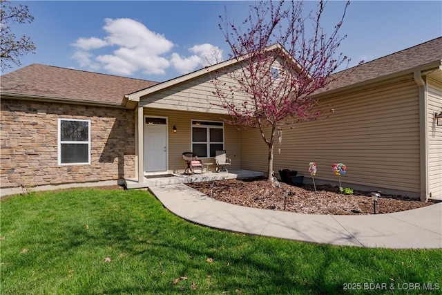 view of front of property with a front lawn, stone siding, and roof with shingles