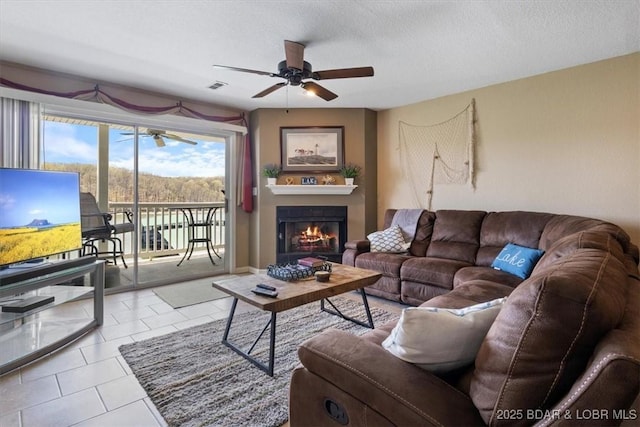 4800 Eagleview Dr Unit 133, Osage Beach, MO 65065 - living room featuring a ceiling fan, a warm lit fireplace, tile patterned floors, and a textured ceiling