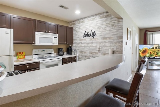 4800 Eagleview Dr Unit 133, Osage Beach, MO 65065 - kitchen featuring white appliances, dark brown cabinetry, wood walls, a breakfast bar area, and recessed lighting