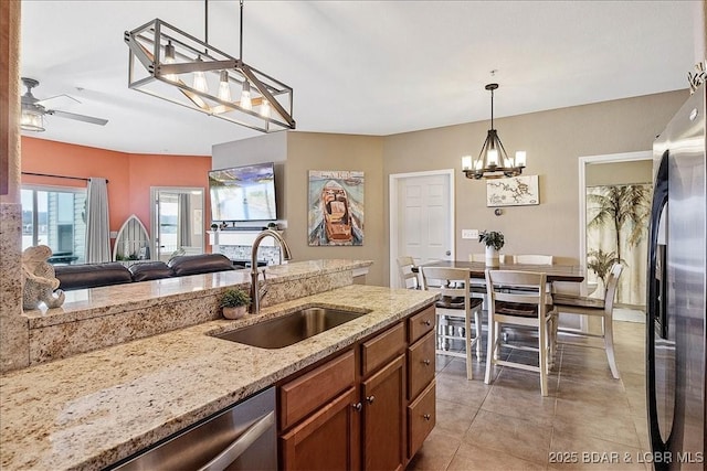 kitchen with light stone counters, a sink, ceiling fan with notable chandelier, brown cabinets, and stainless steel appliances