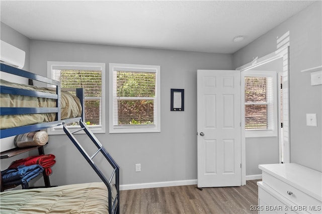 bedroom featuring baseboards, wood finished floors, an AC wall unit, and multiple windows