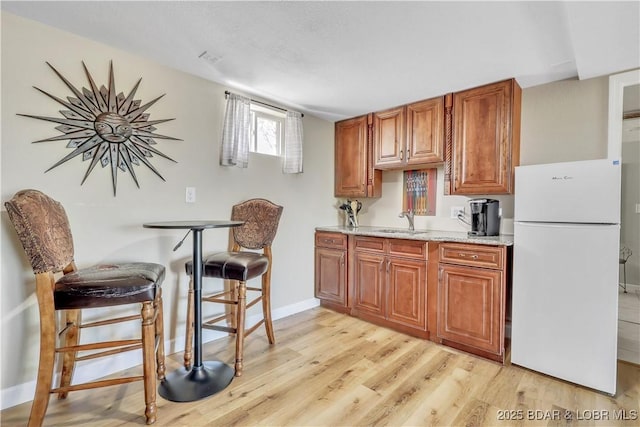 kitchen featuring freestanding refrigerator, brown cabinets, baseboards, and light wood-type flooring