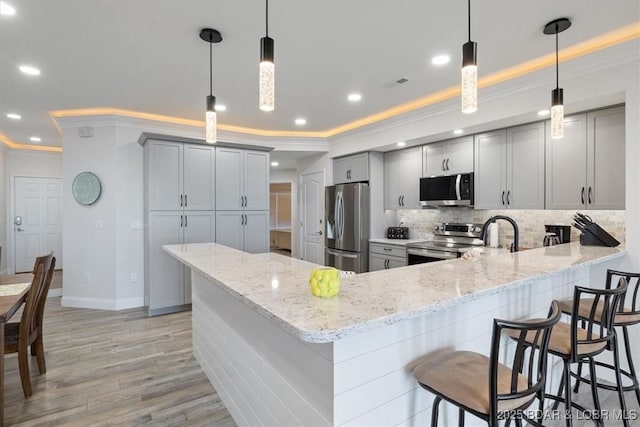 kitchen featuring gray cabinets, appliances with stainless steel finishes, backsplash, a peninsula, and ornamental molding