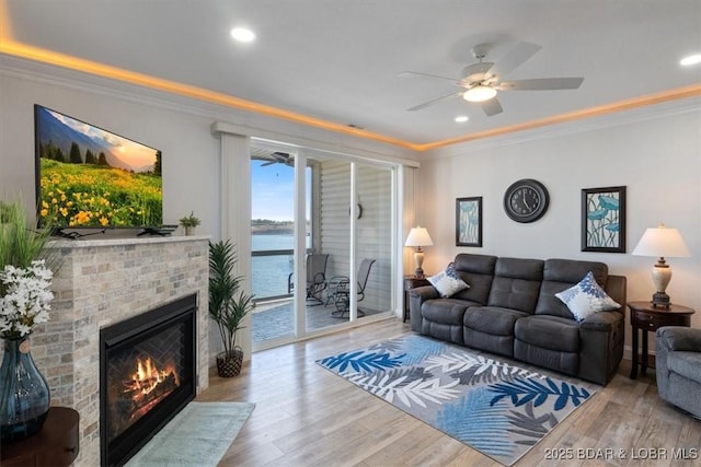 living room featuring a ceiling fan, crown molding, a brick fireplace, and wood finished floors