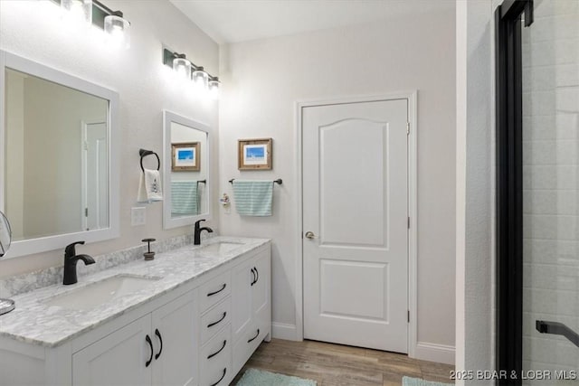 full bathroom featuring baseboards, wood finished floors, a sink, and double vanity