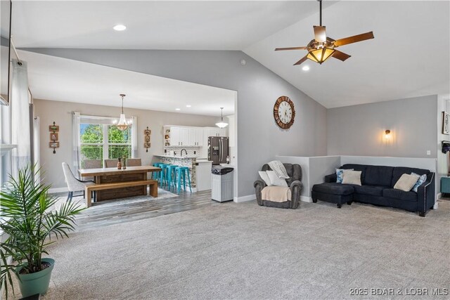 living room with lofted ceiling, light colored carpet, baseboards, recessed lighting, and ceiling fan with notable chandelier