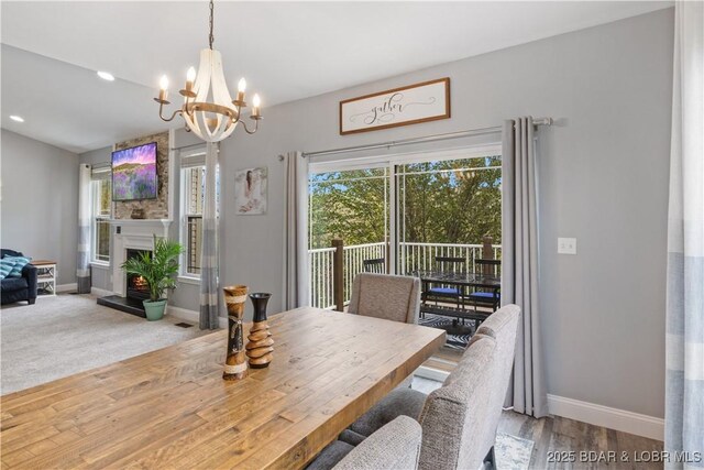 dining space featuring baseboards, a wealth of natural light, a warm lit fireplace, and an inviting chandelier