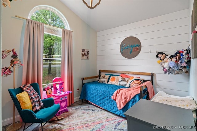 bedroom with baseboards, wood finished floors, wooden walls, and vaulted ceiling