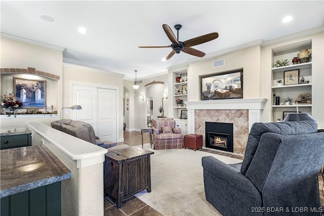 living area with a tile fireplace, built in shelves, ceiling fan, ornamental molding, and arched walkways