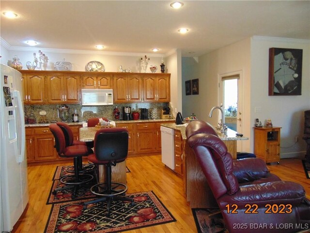 1932 Mimosa Ct, Lebanon, MO 65536 - kitchen featuring white appliances, a kitchen island with sink, brown cabinetry, ornamental molding, and light wood-type flooring
