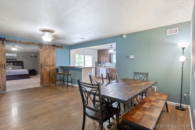 dining area featuring a barn door, a ceiling fan, visible vents, a textured ceiling, and wood finished floors