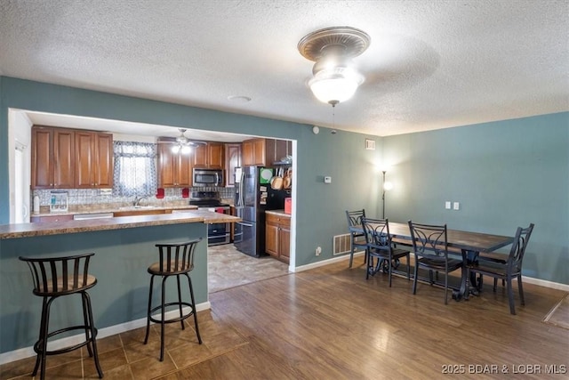 kitchen featuring stainless steel appliances, brown cabinets, ceiling fan, a textured ceiling, and a kitchen breakfast bar