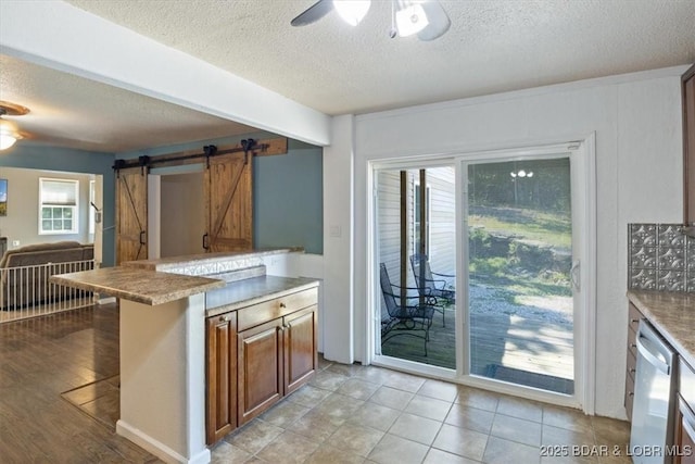 kitchen featuring dishwasher, ceiling fan, a barn door, and a textured ceiling