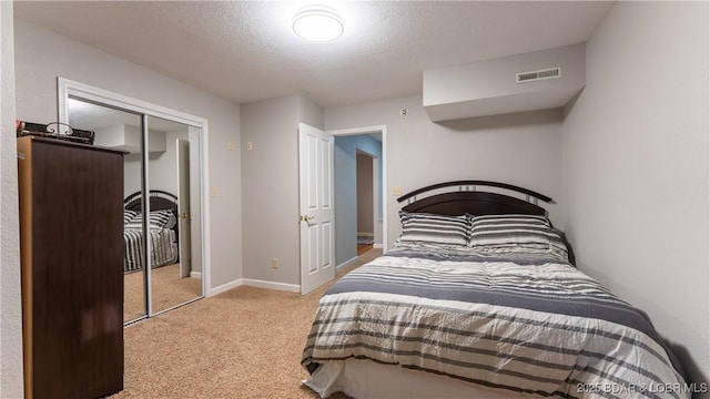 bedroom featuring a closet, light carpet, baseboards, visible vents, and a textured ceiling