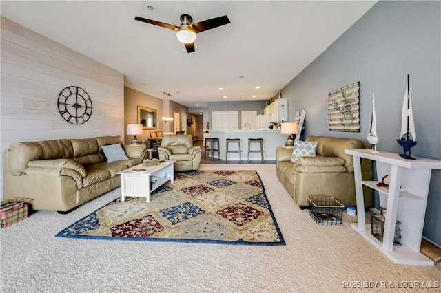 living area with wood walls, a ceiling fan, and carpet flooring