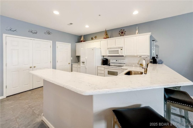 kitchen featuring light stone countertops, a sink, a peninsula, white appliances, and white cabinets