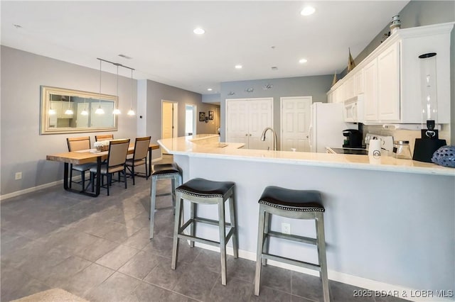 kitchen featuring white appliances, a breakfast bar area, white cabinets, a sink, and baseboards