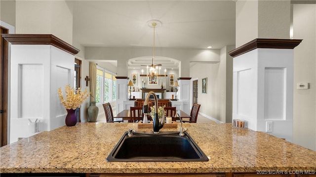kitchen featuring hanging light fixtures, light stone countertops, a chandelier, and a sink