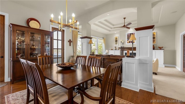 dining area with a raised ceiling, arched walkways, ceiling fan with notable chandelier, baseboards, and wood finished floors