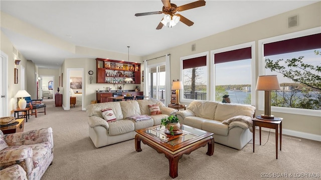 living area featuring indoor wet bar, ceiling fan, light colored carpet, and visible vents