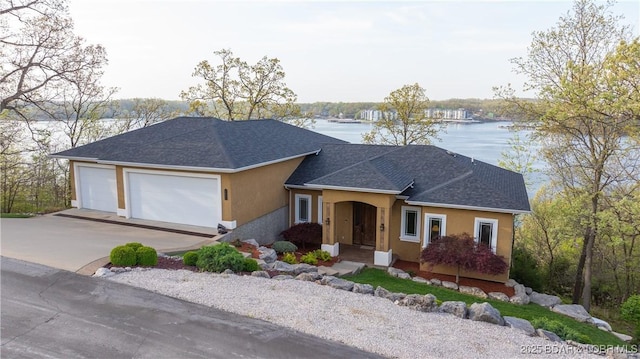 single story home with a shingled roof, an attached garage, stucco siding, a water view, and driveway
