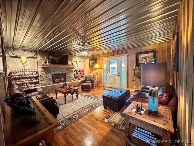 69985 US Highway 50, Tipton, MO 65081 - living room featuring a stone fireplace, wood finished floors, a ceiling fan, wooden walls, and wooden ceiling