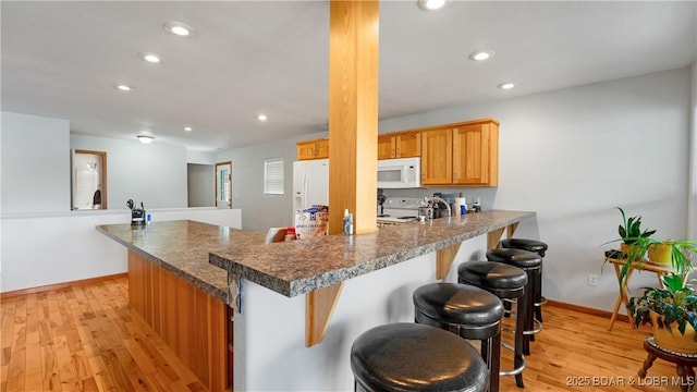 kitchen featuring baseboards, a kitchen bar, recessed lighting, white appliances, and a peninsula