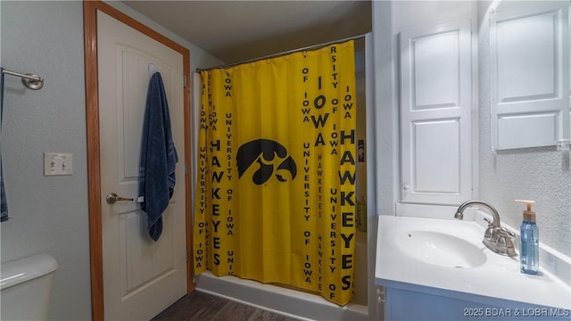 bathroom with wood finished floors, a shower with shower curtain, toilet, a textured wall, and vanity