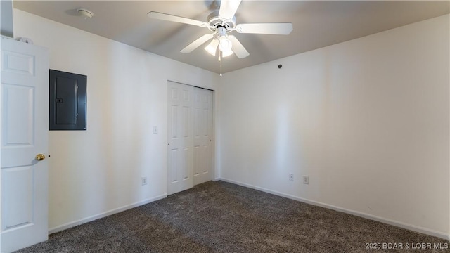 unfurnished bedroom with a closet, electric panel, baseboards, dark carpet, and a ceiling fan