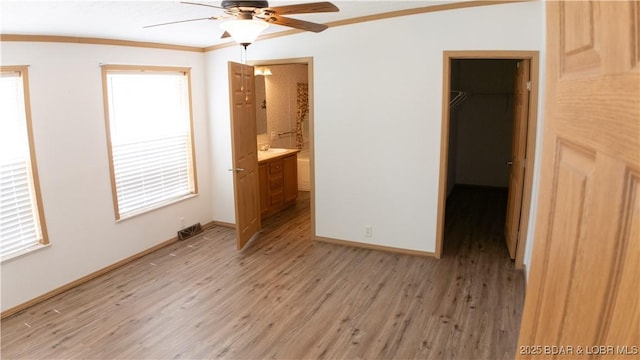 unfurnished bedroom featuring a walk in closet, visible vents, light wood-type flooring, a closet, and ornamental molding