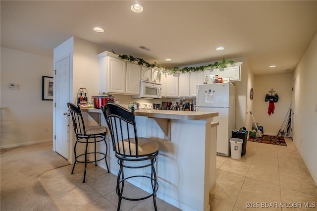 kitchen featuring a peninsula, white appliances, a breakfast bar area, recessed lighting, and white cabinetry