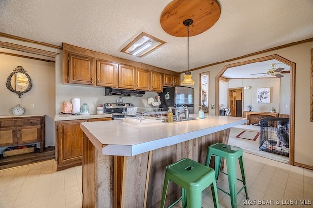 122 Simpson Rd, Urbana, MO 65767 - kitchen featuring appliances with stainless steel finishes, light countertops, brown cabinetry, under cabinet range hood, and ornamental molding