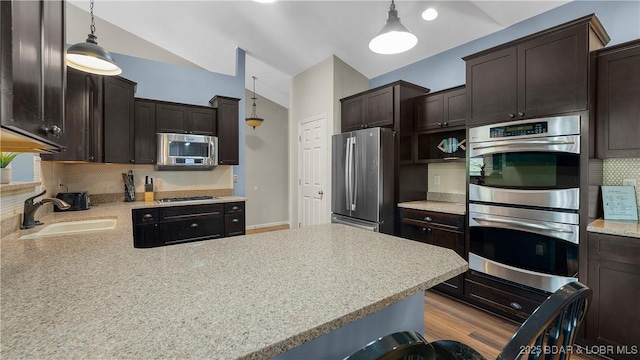 kitchen with decorative backsplash, pendant lighting, appliances with stainless steel finishes, dark brown cabinets, and a sink