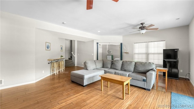 living area with stairs, ceiling fan, baseboards, and light wood-type flooring
