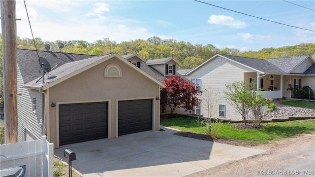 traditional home with roof with shingles, an attached garage, driveway, and stucco siding