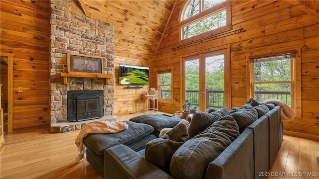 living room with wooden walls, light wood finished floors, a healthy amount of sunlight, and high vaulted ceiling