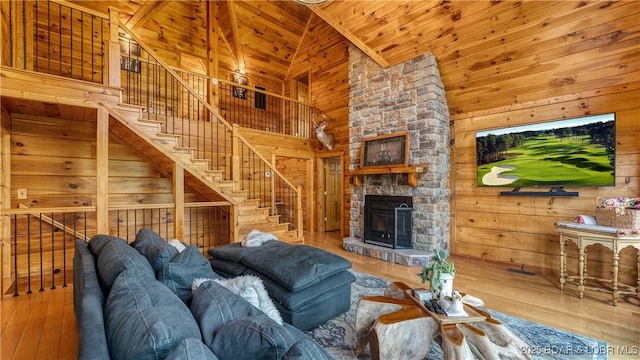 living room with wood-type flooring, high vaulted ceiling, wood walls, and a stone fireplace