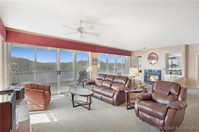 carpeted living room featuring a ceiling fan, a textured ceiling, and a glass covered fireplace