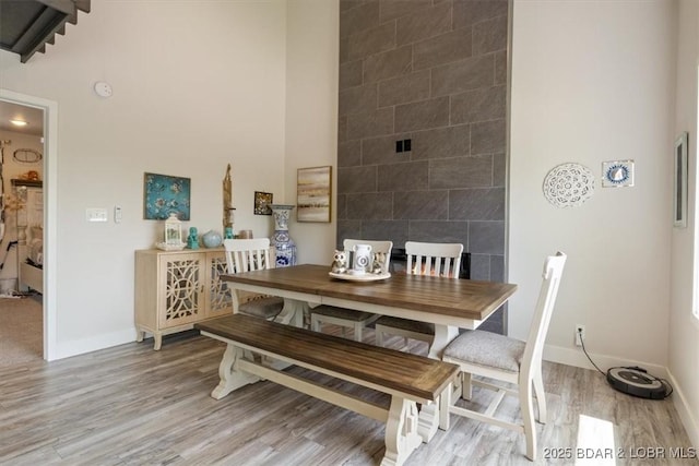 dining area featuring a towering ceiling, baseboards, and light wood-type flooring