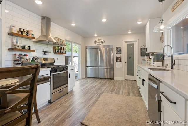 kitchen featuring exhaust hood, appliances with stainless steel finishes, a sink, white cabinets, and light wood-style floors