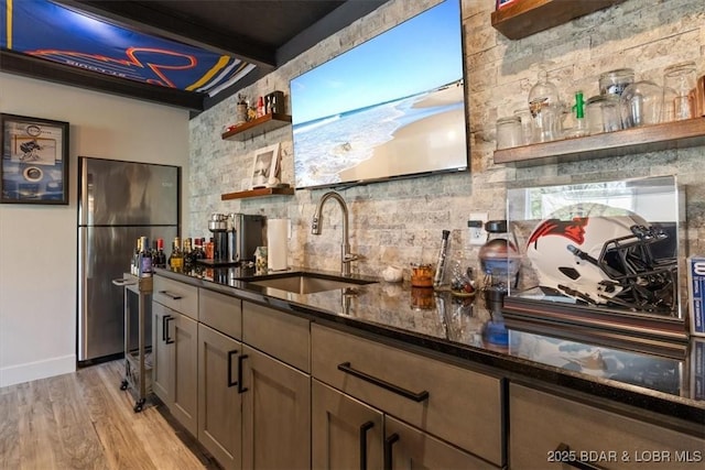 bar with decorative backsplash, a dry bar, a sink, freestanding refrigerator, and light wood finished floors