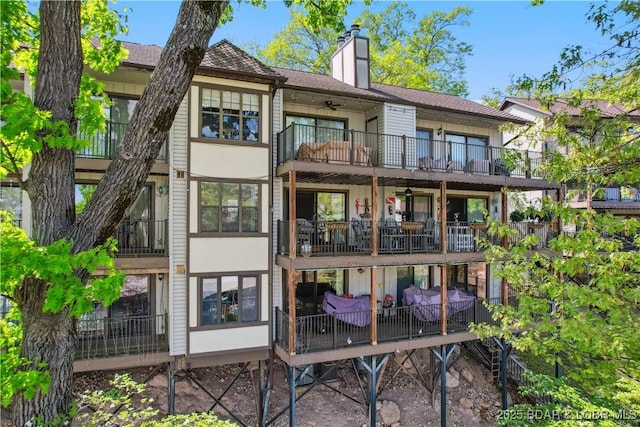 back of property with a ceiling fan, a chimney, and a balcony