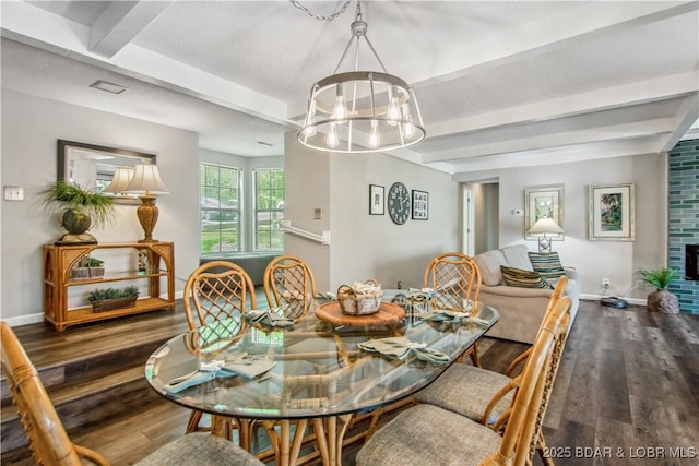 dining area with wood finished floors, a fireplace, beamed ceiling, baseboards, and a chandelier