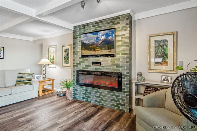 living area with baseboards, beamed ceiling, wood finished floors, and a fireplace