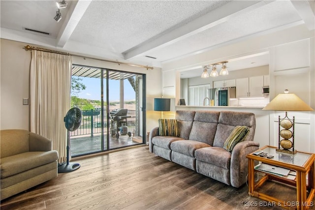 living room featuring wood finished floors, beam ceiling, and visible vents
