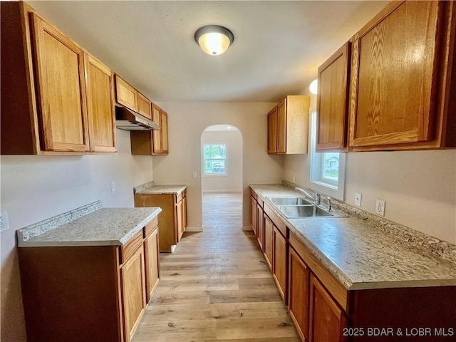 407 Cleveland St, Versailles, MO 65084 - kitchen featuring arched walkways, light wood-type flooring, a sink, light countertops, and under cabinet range hood